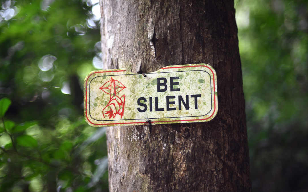 A sign hangs from a tree: be silent please.
